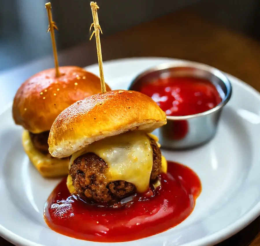 Golden-brown meatball slider bombs on a plate with marinara dipping sauce